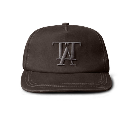 A dark brown structured snapback cap featuring an embroidered tonal gray 'TA' monogram logo on the front, set against a plain white background.